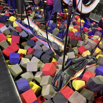 Colorful foam pit with suspended swings above, surrounded by red, yellow, and purple cubes. Vibrant and playful atmosphere.