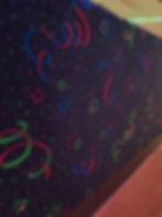 Colorful, retro-patterned carpet with swirling lines, stars, and geometric shapes in a dimly lit room. Bright neon colors create a lively vibe.