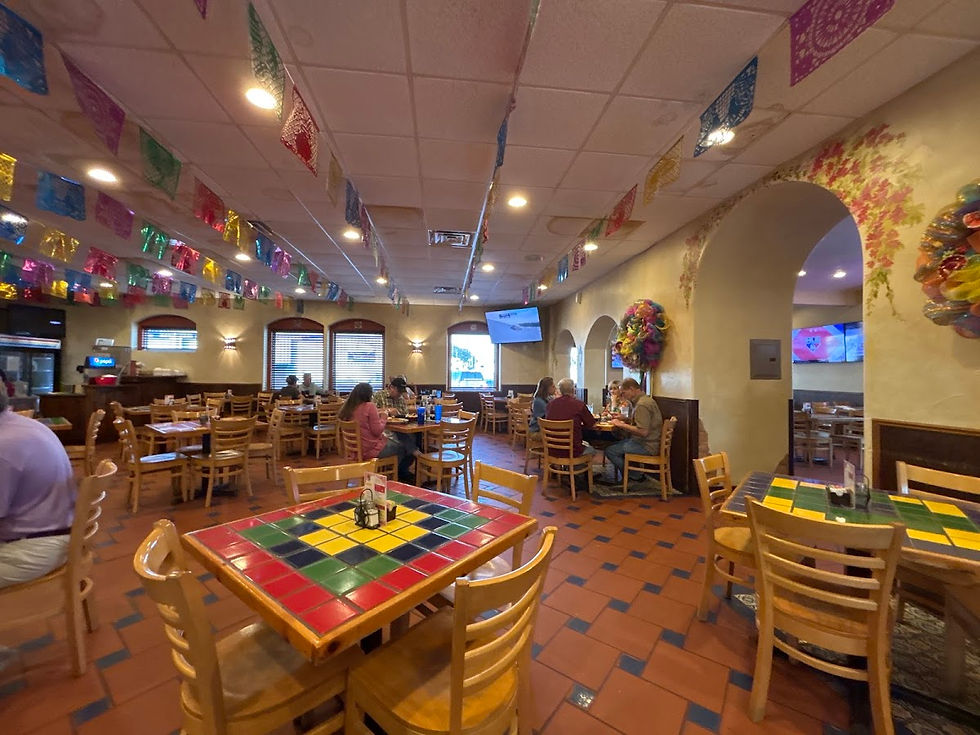 Restaurant interior with people dining, colorful paper flags overhead, and vibrant tile tables. Warm lighting and cheerful atmosphere.