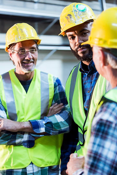 Three workers in hard hats and safety vests talking together at a worksite.