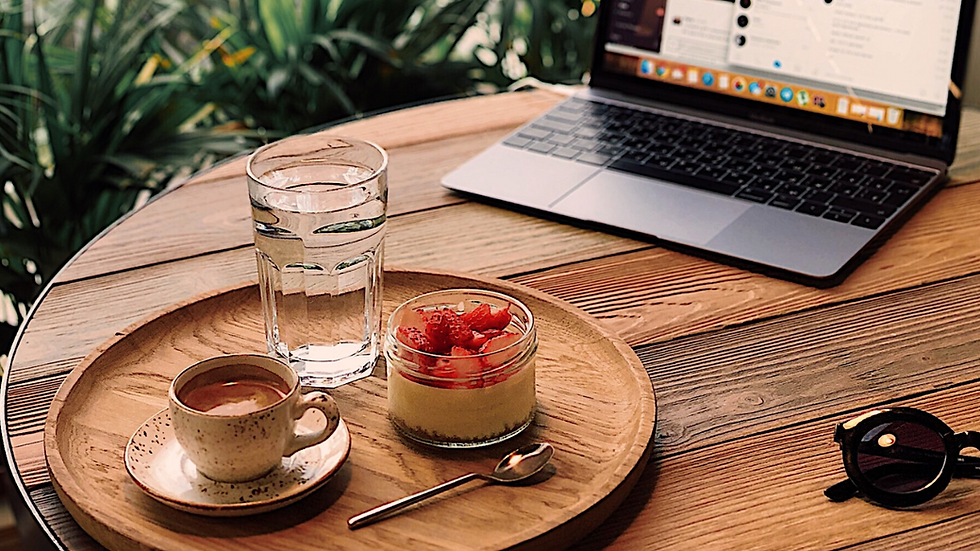 Plateau de pause déjeuner posé sur un bureau en bois, avec une verrine de fruits frais, un verre d’eau, un café et un ordinateur portable en arrière-plan, illustrant une alimentation équilibrée et apaisée en télétravail.