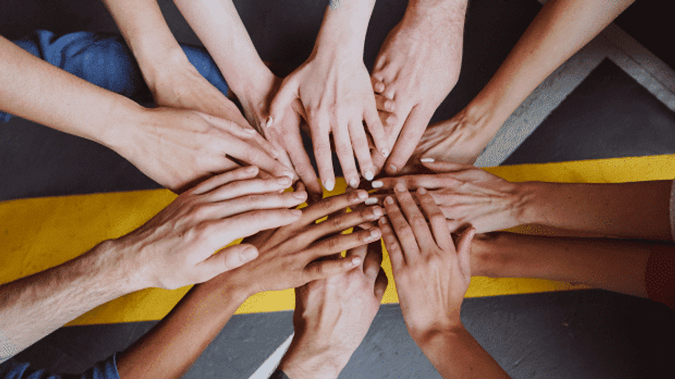 A number of people with out stretching hands, placing them on top of each other, to signify teamwork and collaboration.