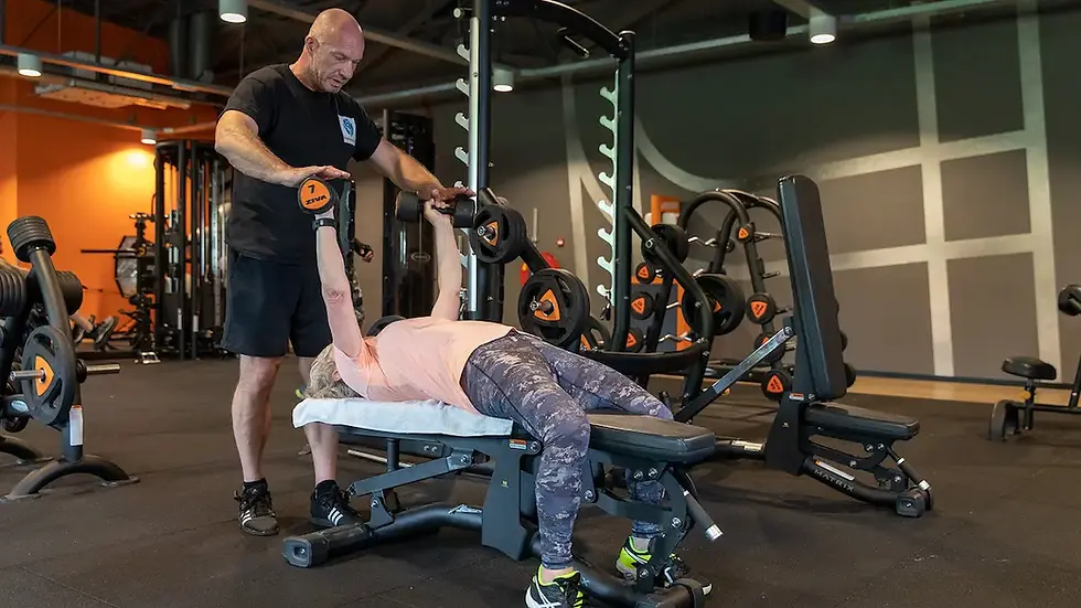Senioren fitnesstraining bij Bodyformation Rotterdam: vrouw voert dumbbell bench press uit onder begeleiding van personal tra