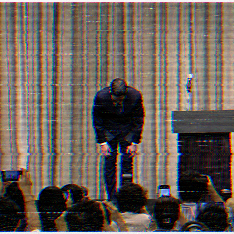Shinsegae chairman Chung Yong-jin bends in a deep public-apology bow at a podium with a microphone, photographed by a crowd holding up phones, against a dark pleated stage curtain.