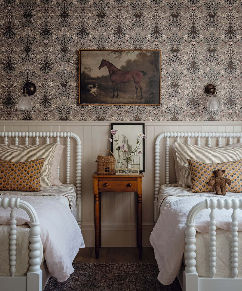 Twin beds with striped and floral pillows in a vintage room. Horse painting on floral wallpaper. Wooden nightstand with flowers. Cozy vibe.