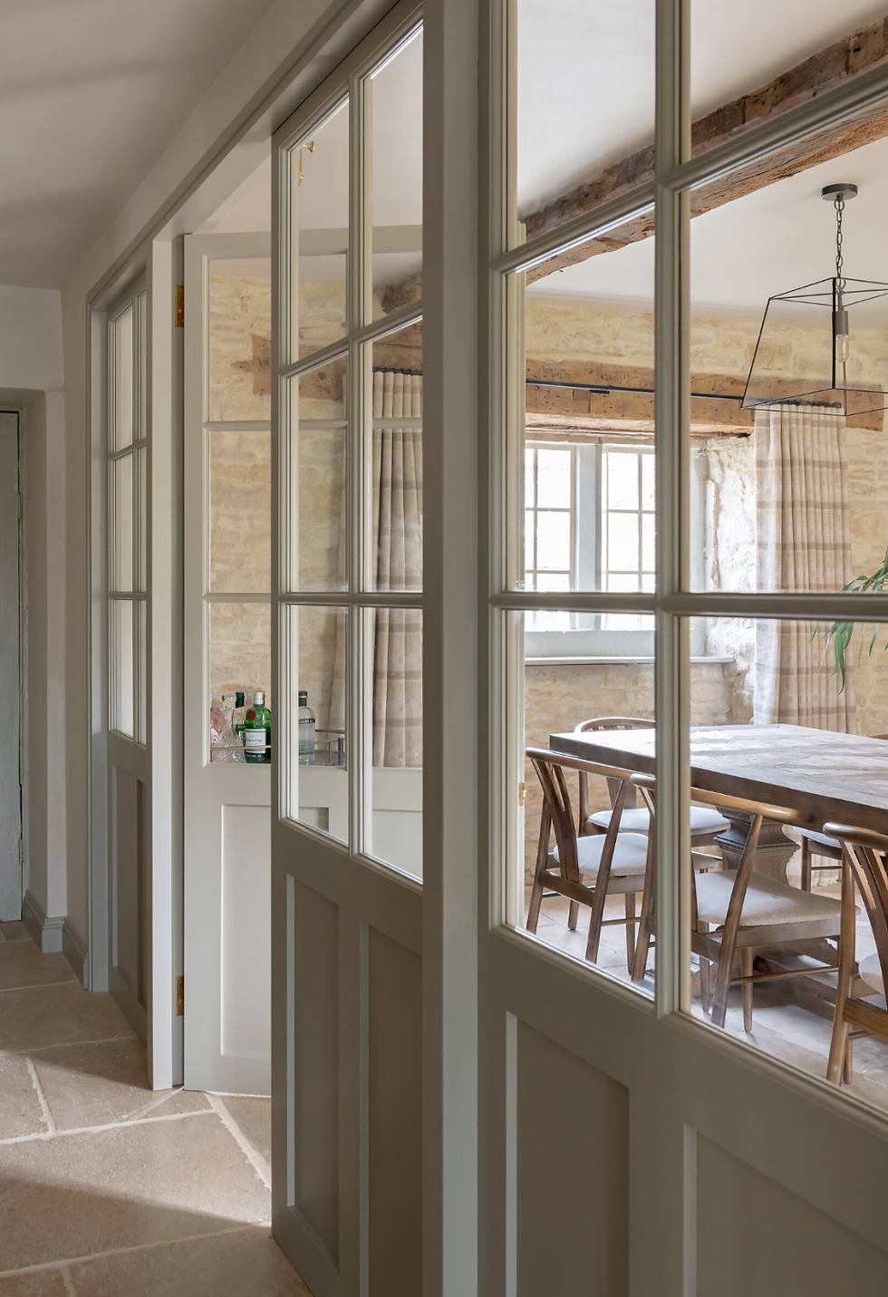 Glass-paneled doors leading to a sunlit dining room with a wooden table and chairs. Stone walls and neutral tones create a warm atmosphere.