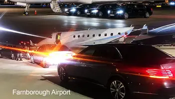     Luxury chauffeur cars lined up beside a private jet at Farnborough Airport at night.  Dinez Official Logo with the Tripadvisor Awards.  Timing Perfected. Luxury Chauffeur Service