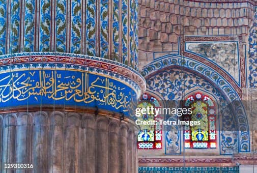 Close-up inside the Blue Mosque showing a fluted stone column wrapped with a blue band of Arabic calligraphy beside an arched wall with blue floral patterns and stained glass windows. A Getty Images watermark overlays the center with the text "gettyimages" and "Credit.