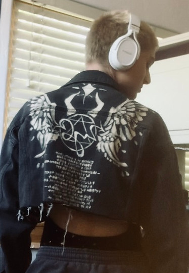 person wearing jacket painted with angel wings, horns, a symbol, and runes