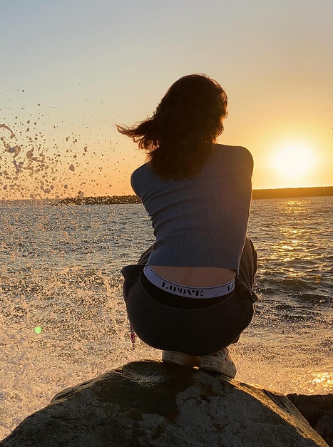 girl sitting on a rock in front of the ocean at sunset