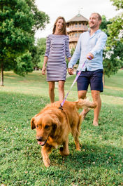Man and woman walking Golden Retriever on a leash in front of Patterson Park's Pagoda in Baltimore city. g man and woman on the grass in a city park.