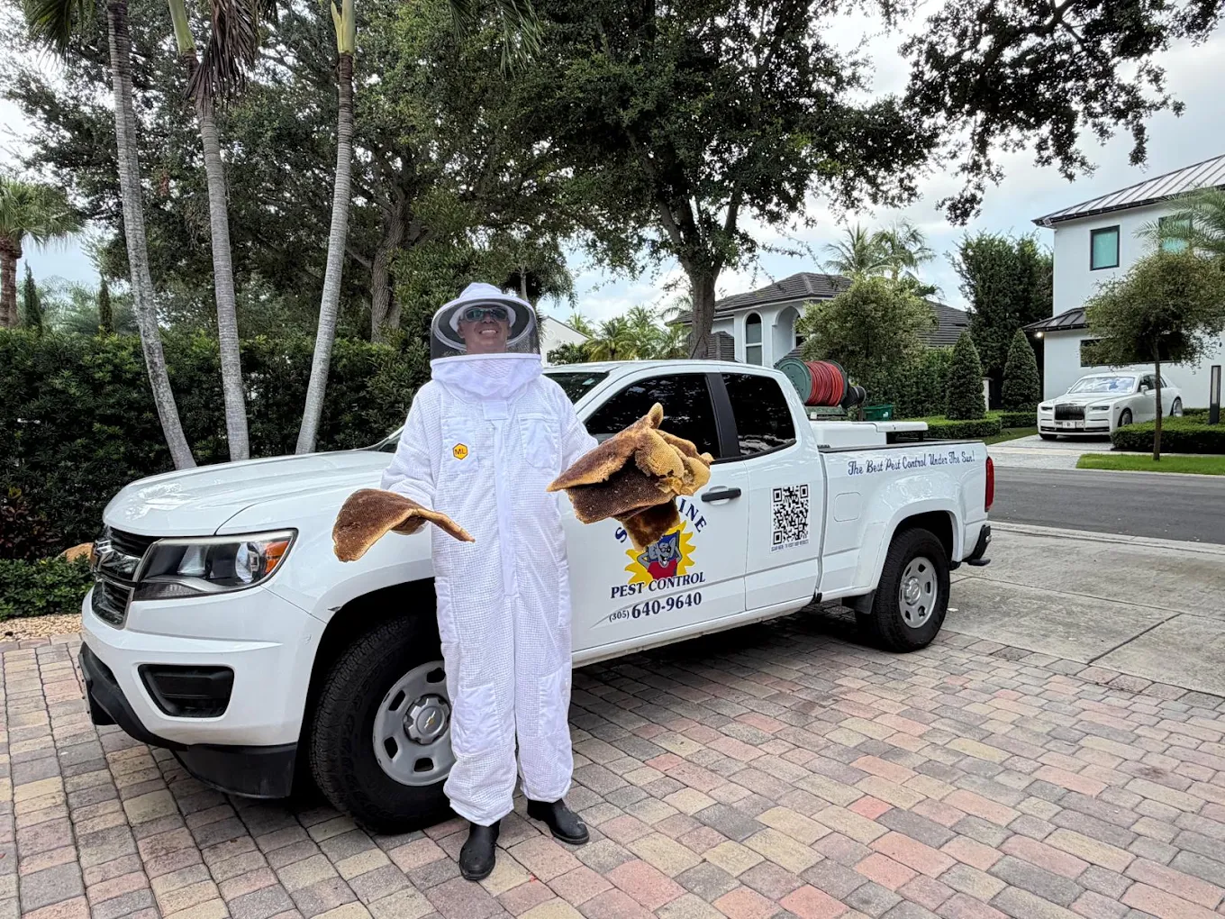 Bee removal in Miami, Sunshine Pest Control technician in a bee suit with honeycomb by the company truck