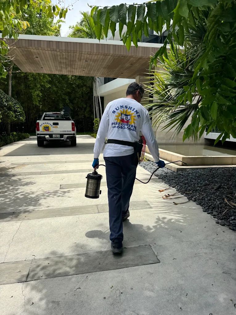 Sunshine Pest Control technician with sprayer and company truck at a Miami home