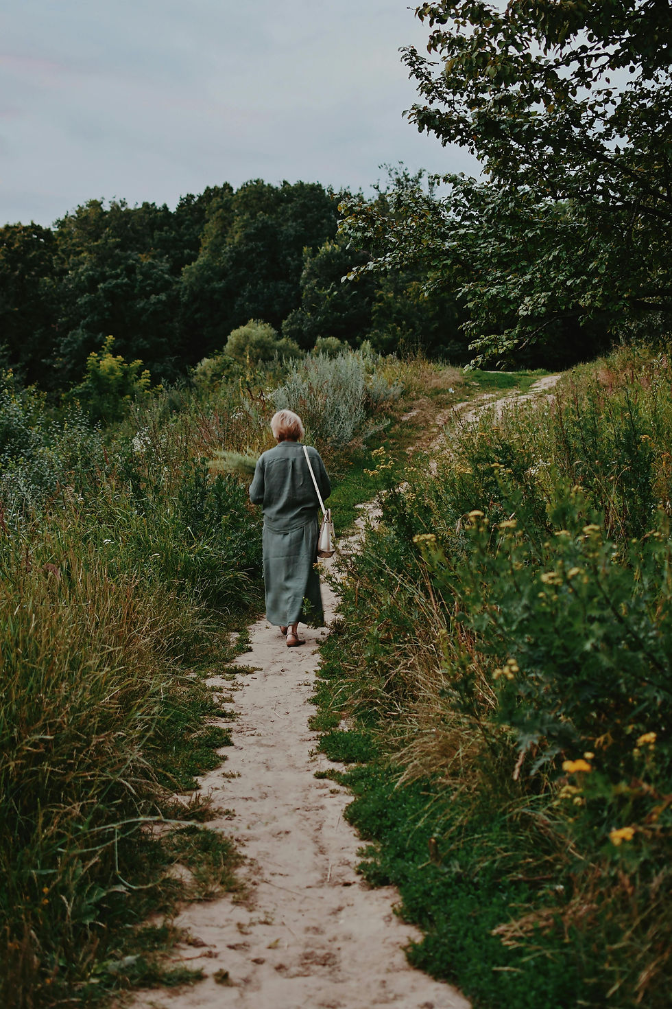 une femme de cinquante ans qui se promène dans la nature en portant une robe chemise longue et ample, en coton kaki