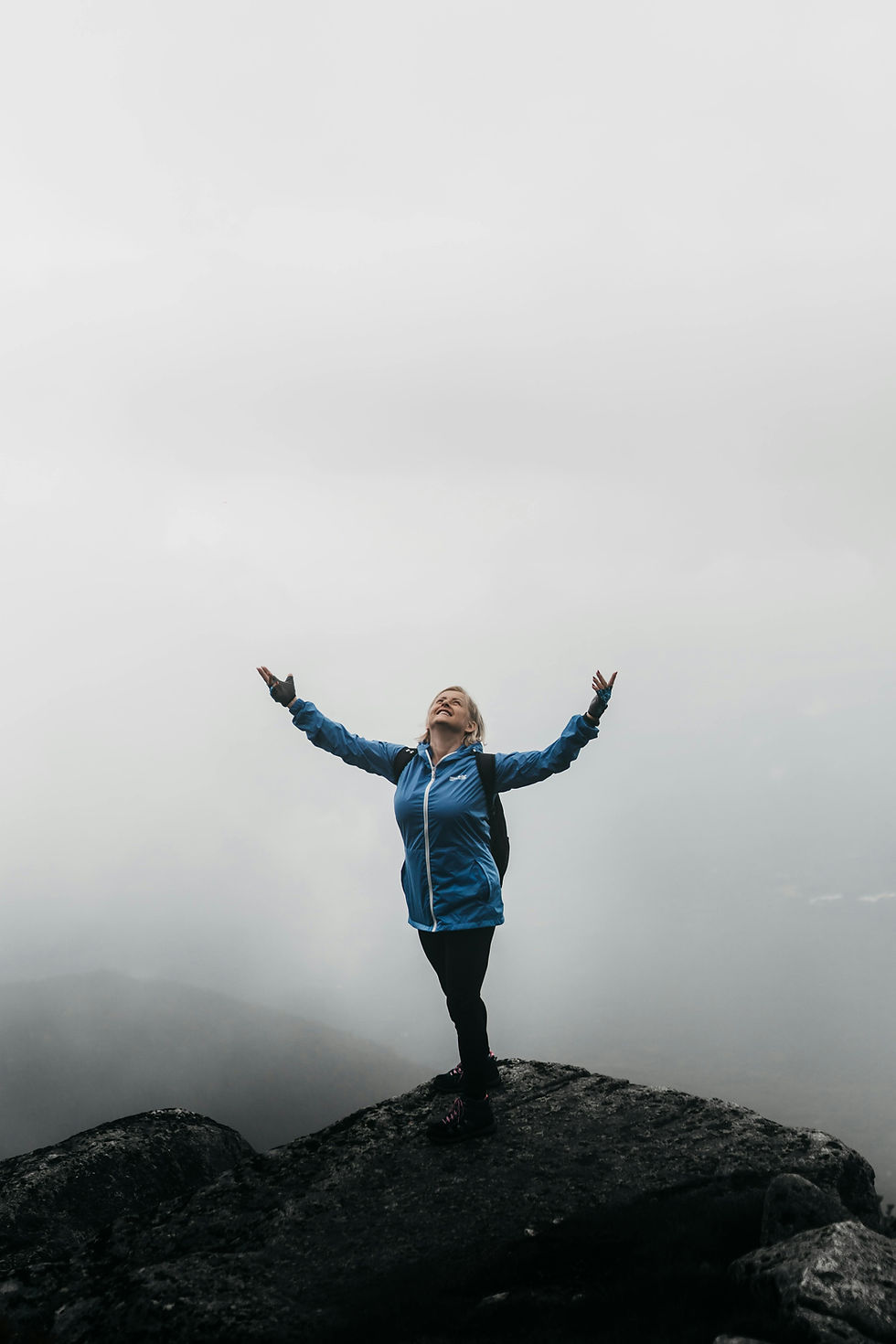 une femme de cinquante ans qui a gravit une montagne,arrivée au sommet, elle lève les bras et les mains en signe de victoire et elle sourit