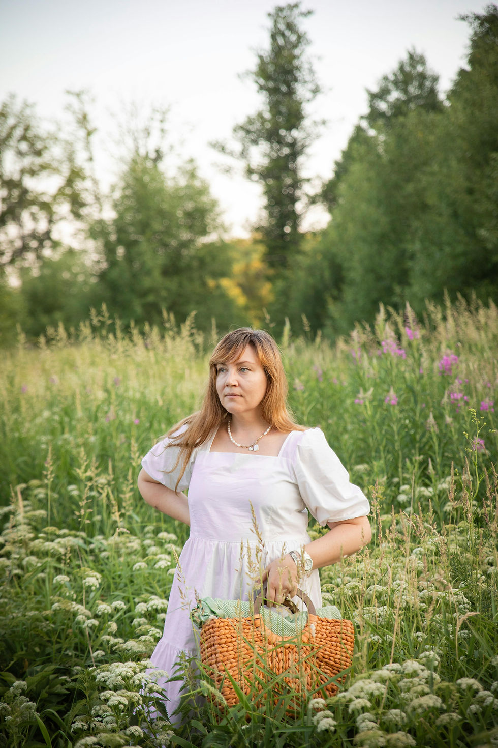 une femme de cinquante ans qui marche dans la nature au milieu des fleurs, elle porte une belle robe en coton clair ample version cottagecore et elle a un panier dans la main