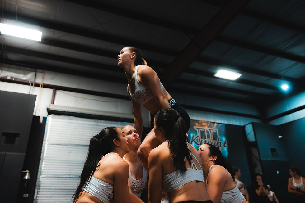 Bases preparing a cheerleading stunt with the flyer during a team training session.