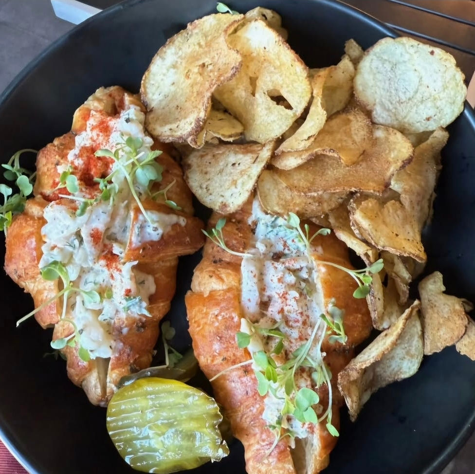 a black plate topped with croissants and potato chips