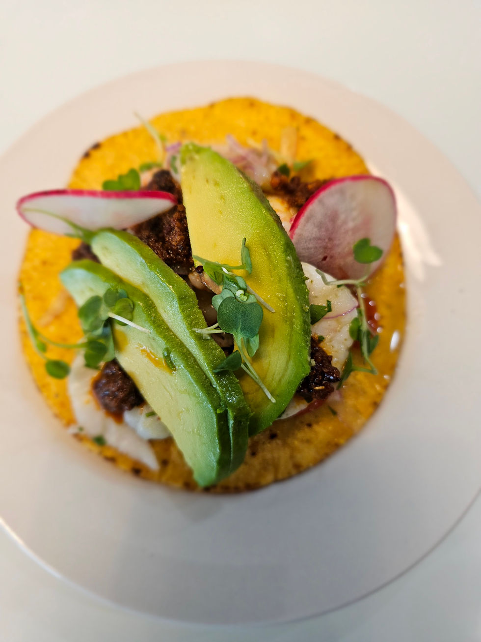 a taco with avocado and radishes on a white plate