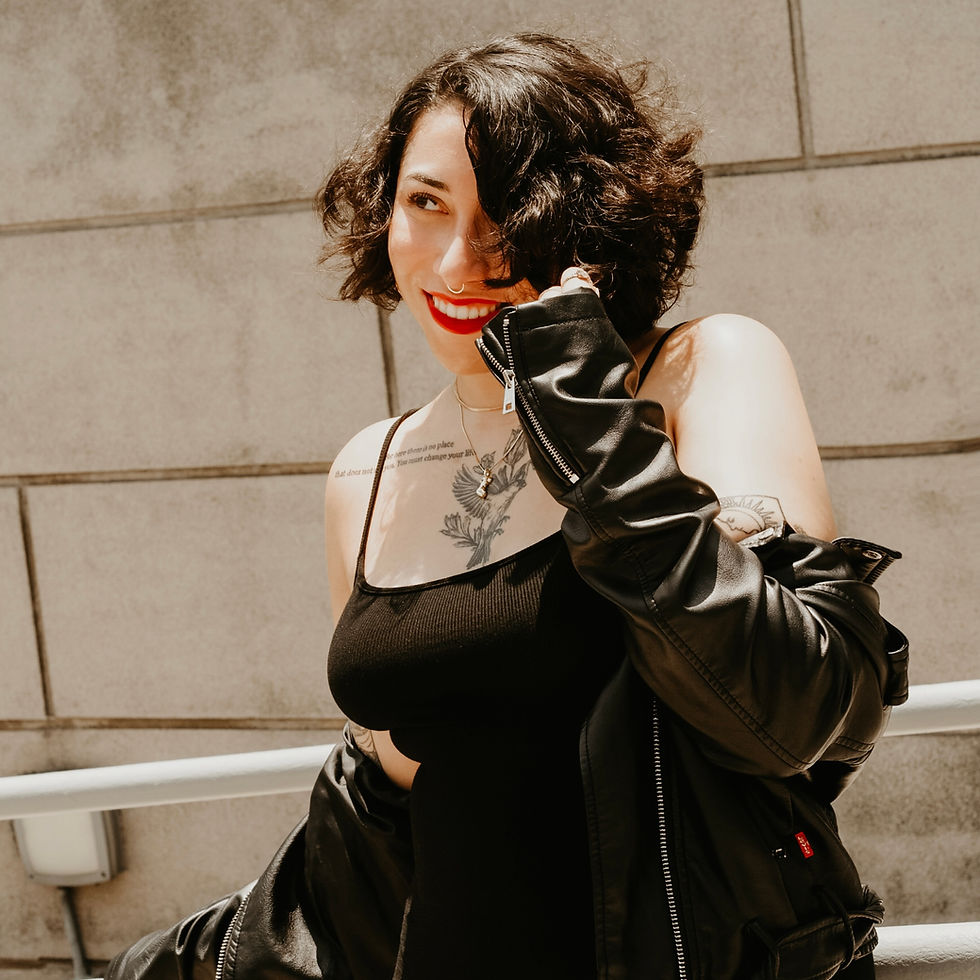 Fatimah Asghar in peach dress holds yellow rose, sitting amid vibrant flowers. Star earrings, henna tattoos, and ornate drapery create an artistic mood.