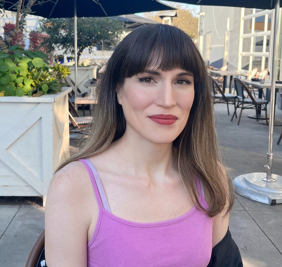 Fatimah Asghar in peach dress holds yellow rose, sitting amid vibrant flowers. Star earrings, henna tattoos, and ornate drapery create an artistic mood.