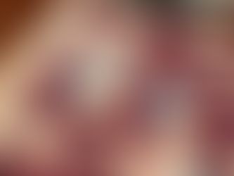 A close-up of a Scrabble board mid-game, maroon tiles spelling words like “TAXING,” “TEDDY,” and “COILY,” with the edge of the game box and books visible on a wooden table.