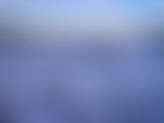 Waves crash gently on a rocky shore at sunset, with soft foam rolling toward the camera. In the distance, low forested islands and mountain silhouettes sit beneath a pastel sky of blue and peach—capturing the quiet beauty and emotional power of the ocean.