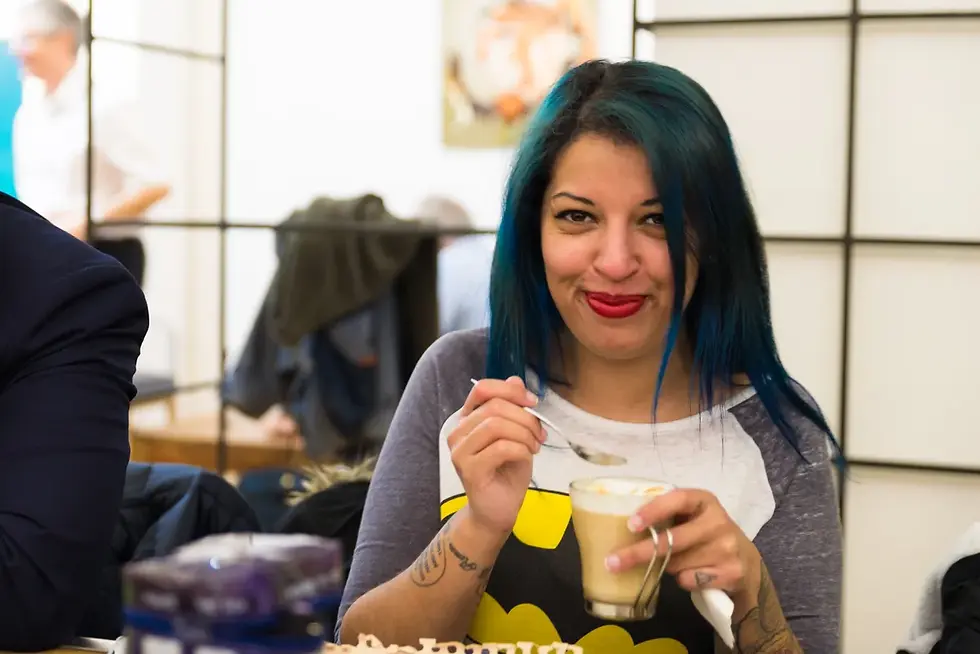 Photographe événementiel Chambéry - une femme souriante avec des cheveux bleus tient une tasse de café. Elle porte un haut à motif Batman dans un café lumineux.