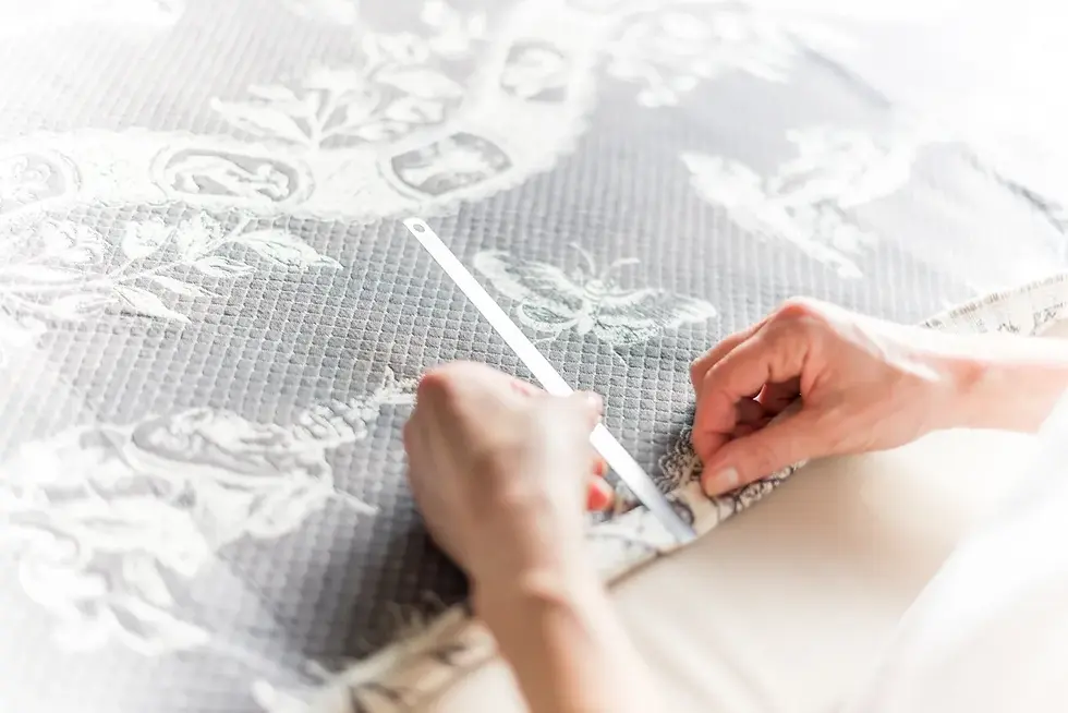 Photographe Annecy - Mains ajustant un tissu gris à motifs floraux avec une règle, lumière douce, ambiance paisible.