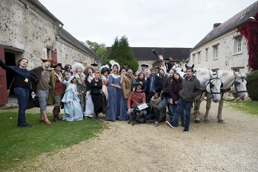 Photographe tournage cinéma Annecy - photo d'équipe de film pose joyeusement devant un bâtiment rustique. Atmosphère festive et costumée.