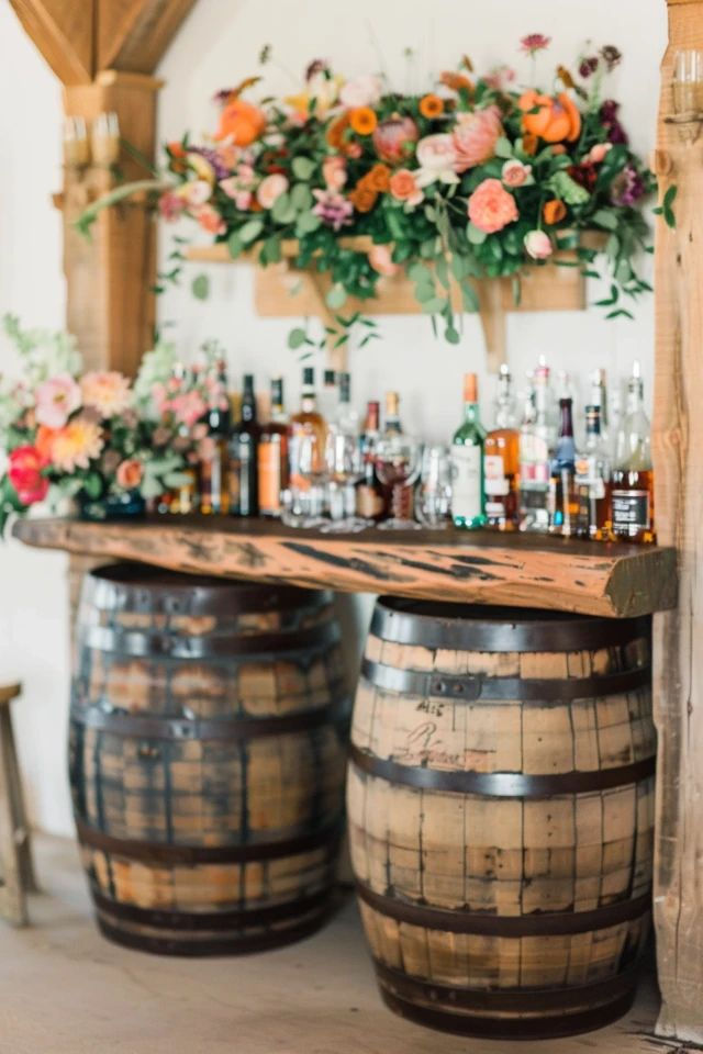 A charming bourbon barrel bar elegantly adorned with vibrant floral arrangements sets a rustic yet sophisticated atmosphere for a wedding celebration.