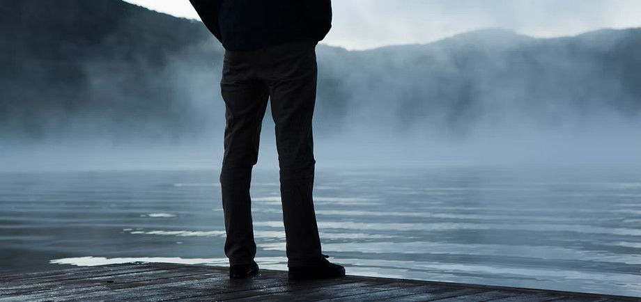 man standing by the edge of a foggy lake