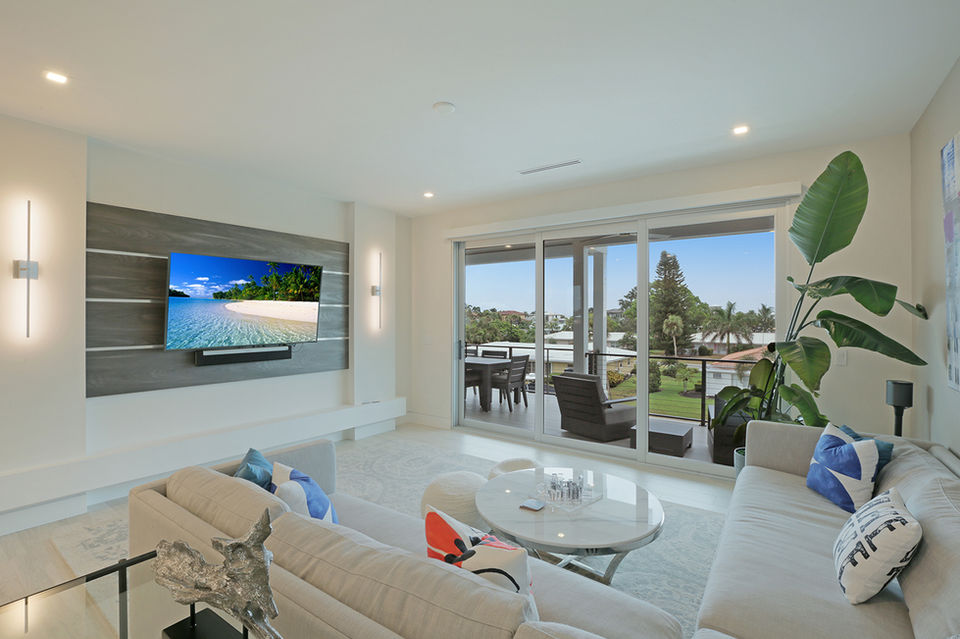 Coastal-style living room with large sliding glass doors, modern TV wall, and balcony view by REGIUS in Florida.
