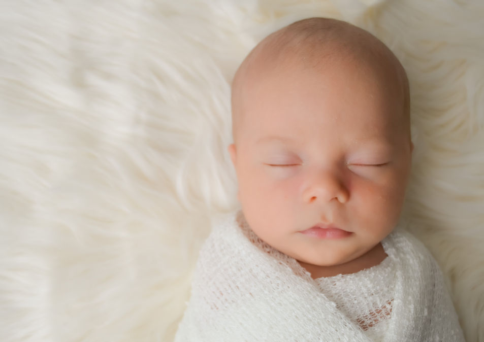 Close-up of a newborn baby boy wrapped in a soft white wrap, resting on fluffy flokati fabric