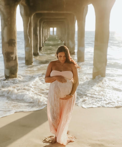 Mother-to-be standing in a golden hour beach, glowing in a flowing gown, embodying grace and beauty