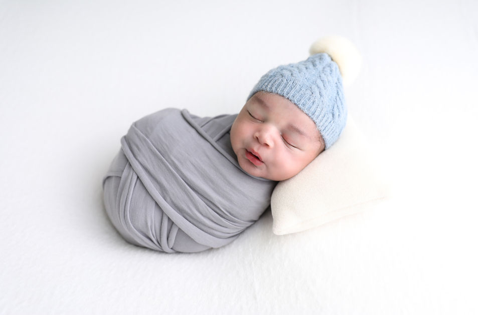 Newborn baby boy wrapped in a soft gray wrap, wearing a cozy blue knit hat during a studio photoshoot in Torrance, CA