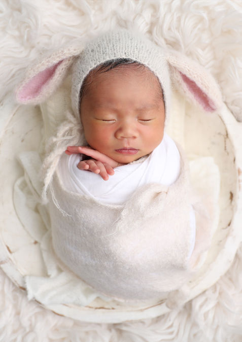 Newborn baby in a wooden bowl wearing a bunny ears bonnet