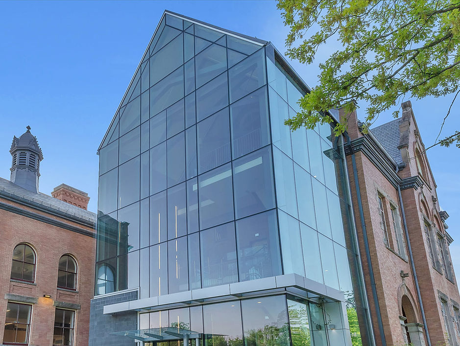 Modern glass facade connecting two historic brick buildings under blue sky, fully clad in glass by Southwest Doors & Hardware