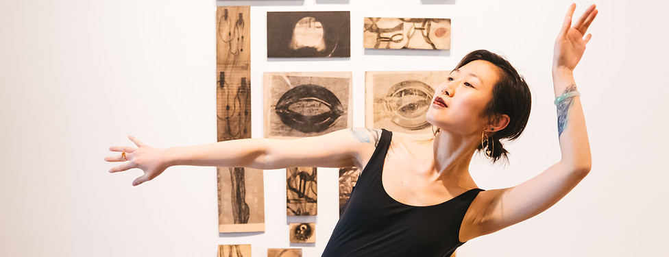 Poet Anis Gisele posing with her arms. Artwork in the background by Leah Gerrard. Photo by Sunita Martini.