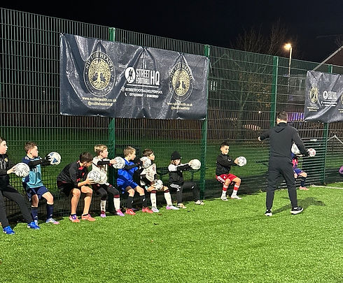 Young football players holding footballs in line during evening training session