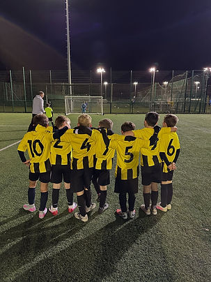 Young footballers wearing yellow kits standing together in huddle on pitch