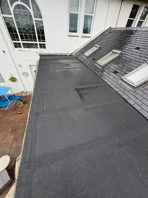 Newly installed black flat felt roof on a property adjacent to pitched slated roofs and windows