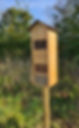 Tall wooden solitary bee house installed on a timber post in a green grassy garden area