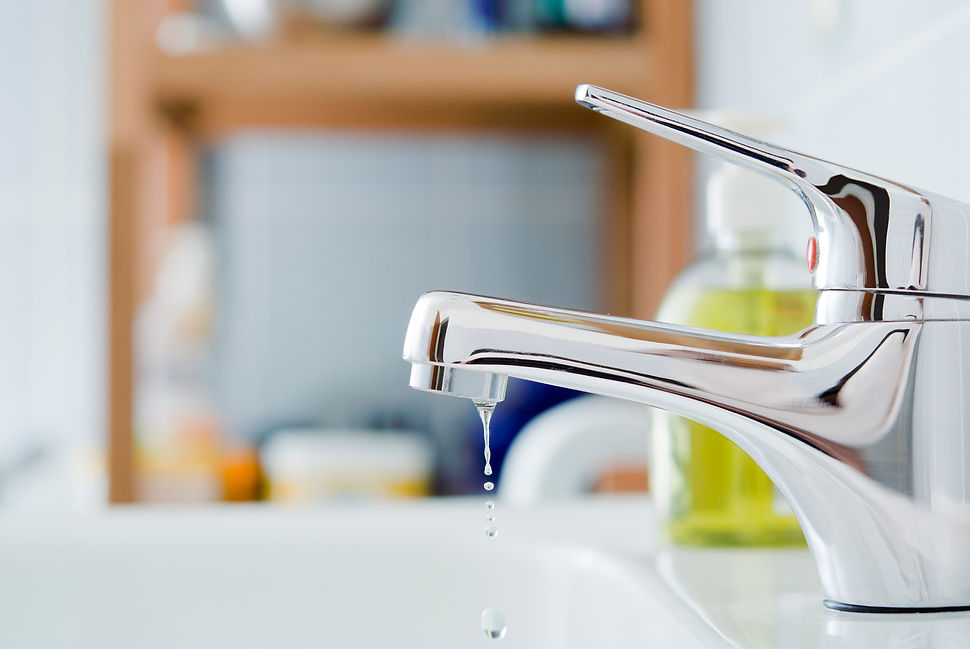 Water dripping from modern chrome mixer tap into white basin