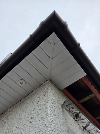 Looking up at clean white uPVC soffits and dark guttering installed on a roof corner