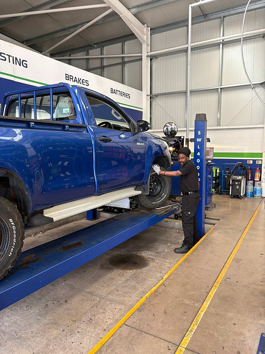 Blue pickup truck raised on a hydraulic lift in a garage workshop with a mechanic standing nearby