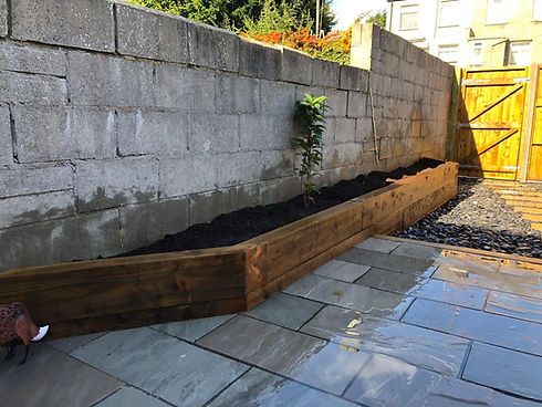 Paved patio area with stone retaining wall and raised garden sleeper bed