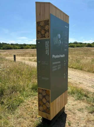 Tall dark grey metal wayfinding sign post on a gravel pathway