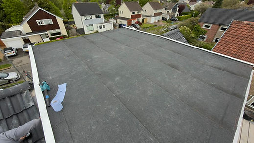 Aerial view of a flat felt roof installation overlooking residential houses in the background