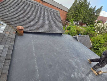 A flat roof covered with black roofing felt or membrane, adjacent to pitched tile roofs on a residential property.